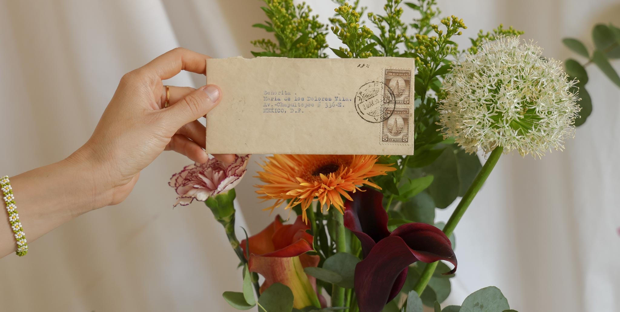 Hand holding a vintage envelope with floral arrangement and postmark against a neutral background. Join the newsletter — Florilegium Paris