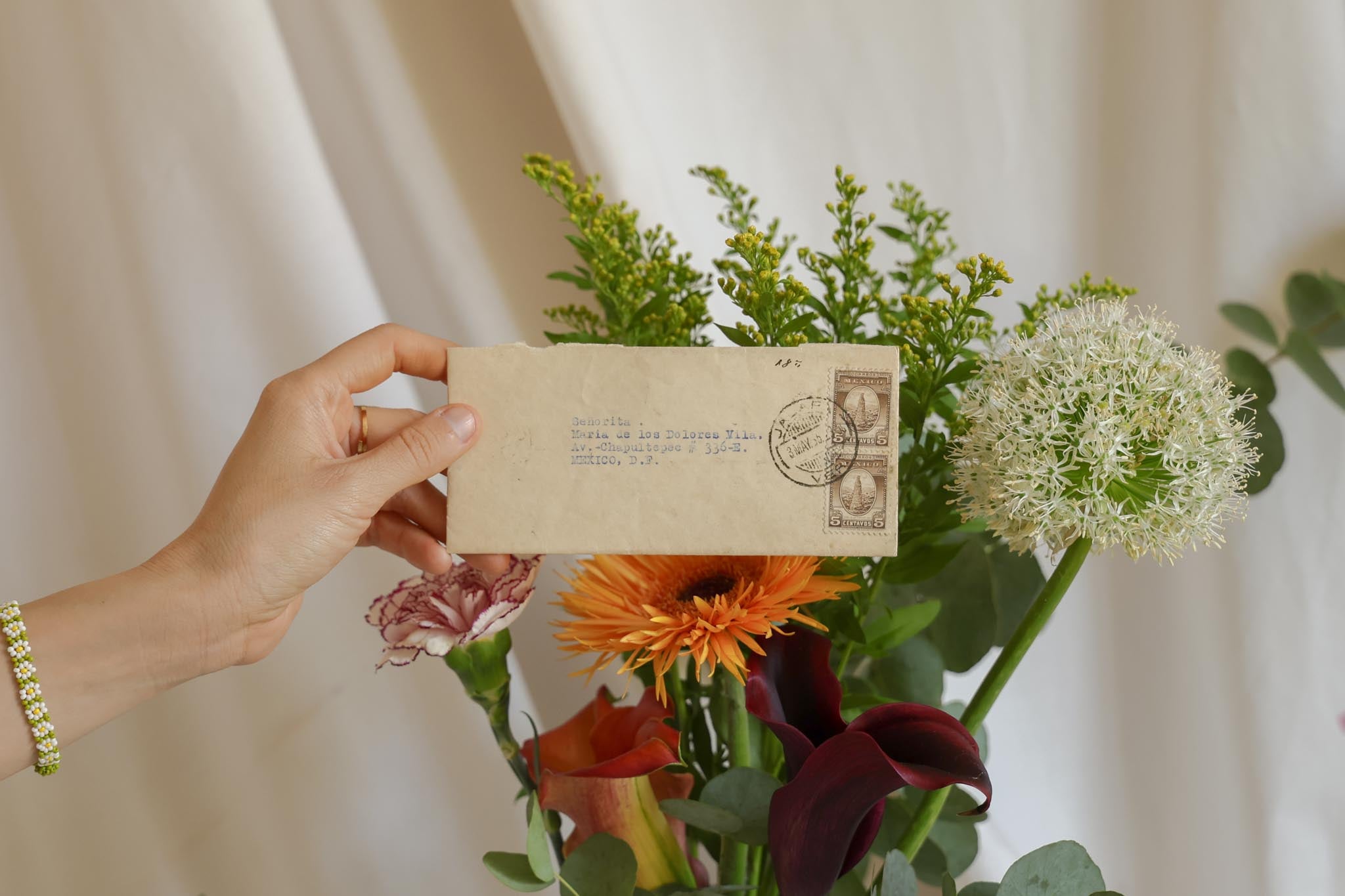 Hand holding a vintage envelope with floral arrangement and postmark against a neutral background. Join the newsletter — Florilegium Paris
