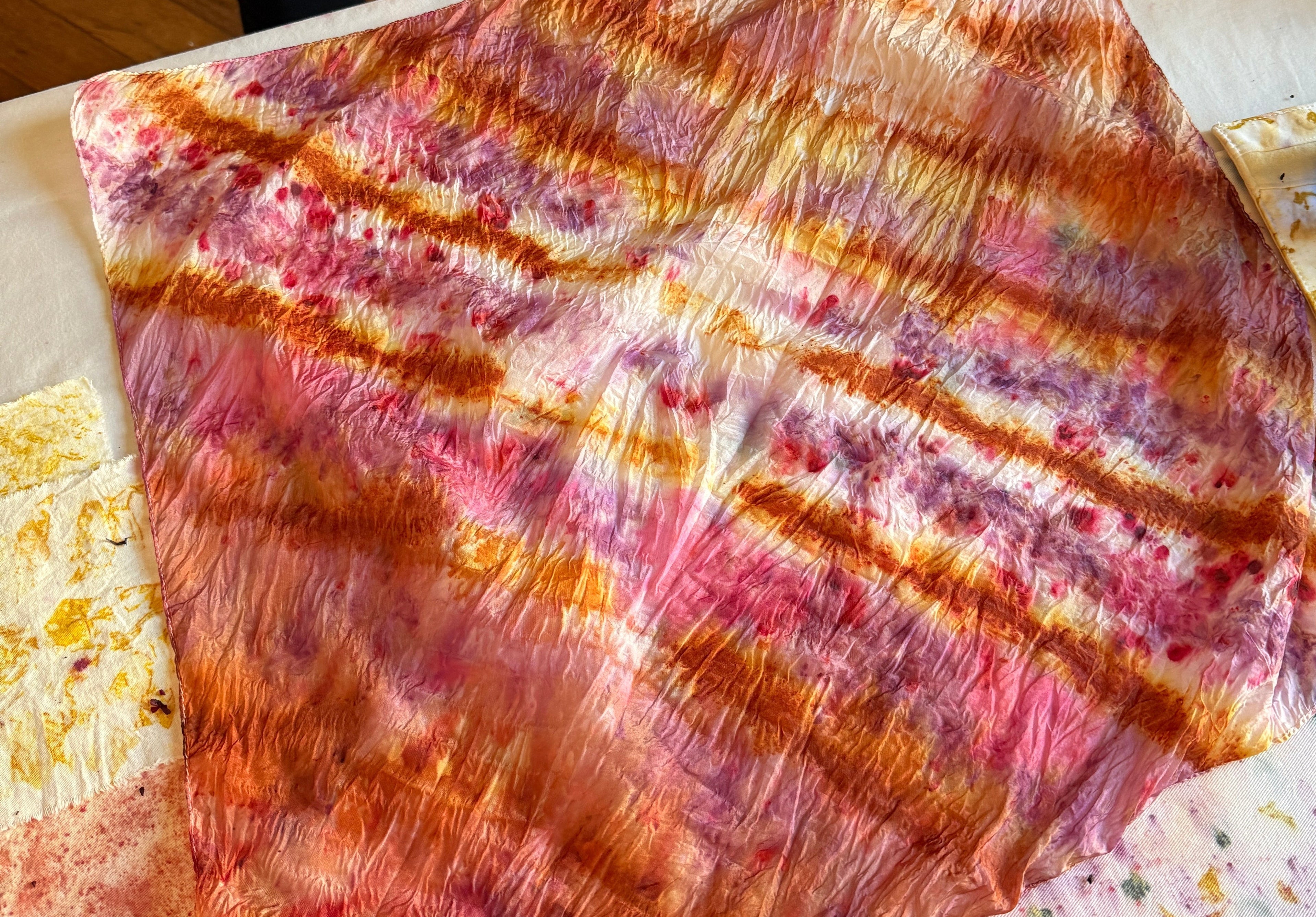 Colorful tie-dye with natural dyes fabric on a white surface with some yellow and red patterns.